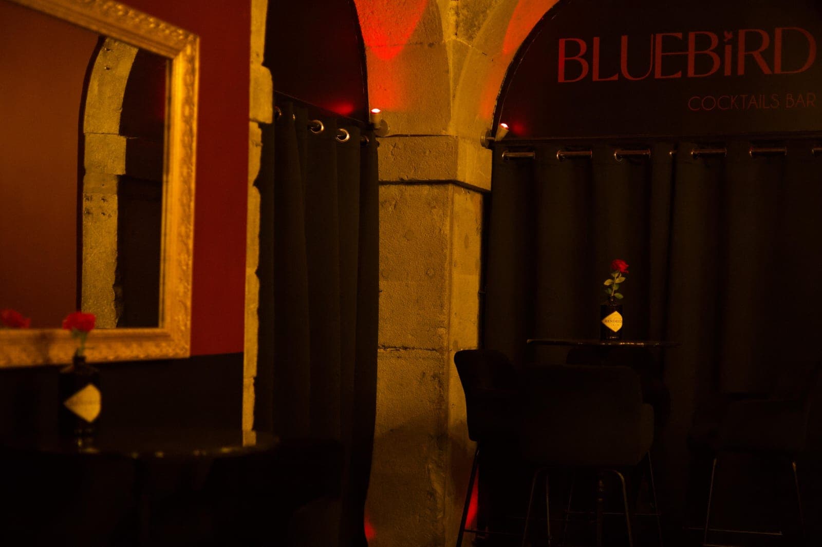 Alcôve du Bluebird : voûtes de pierre, rideaux sombres et enseigne lumineuse