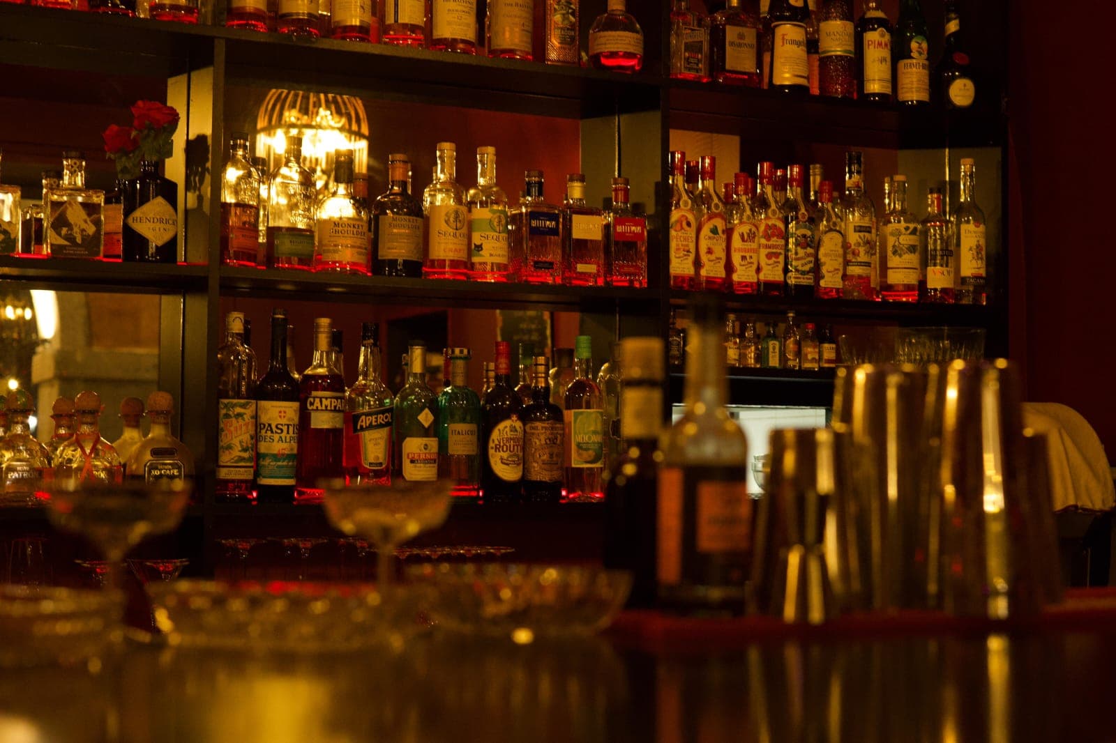 Étagères du bar garnies de bouteilles de whisky et coupes à cocktail au premier plan