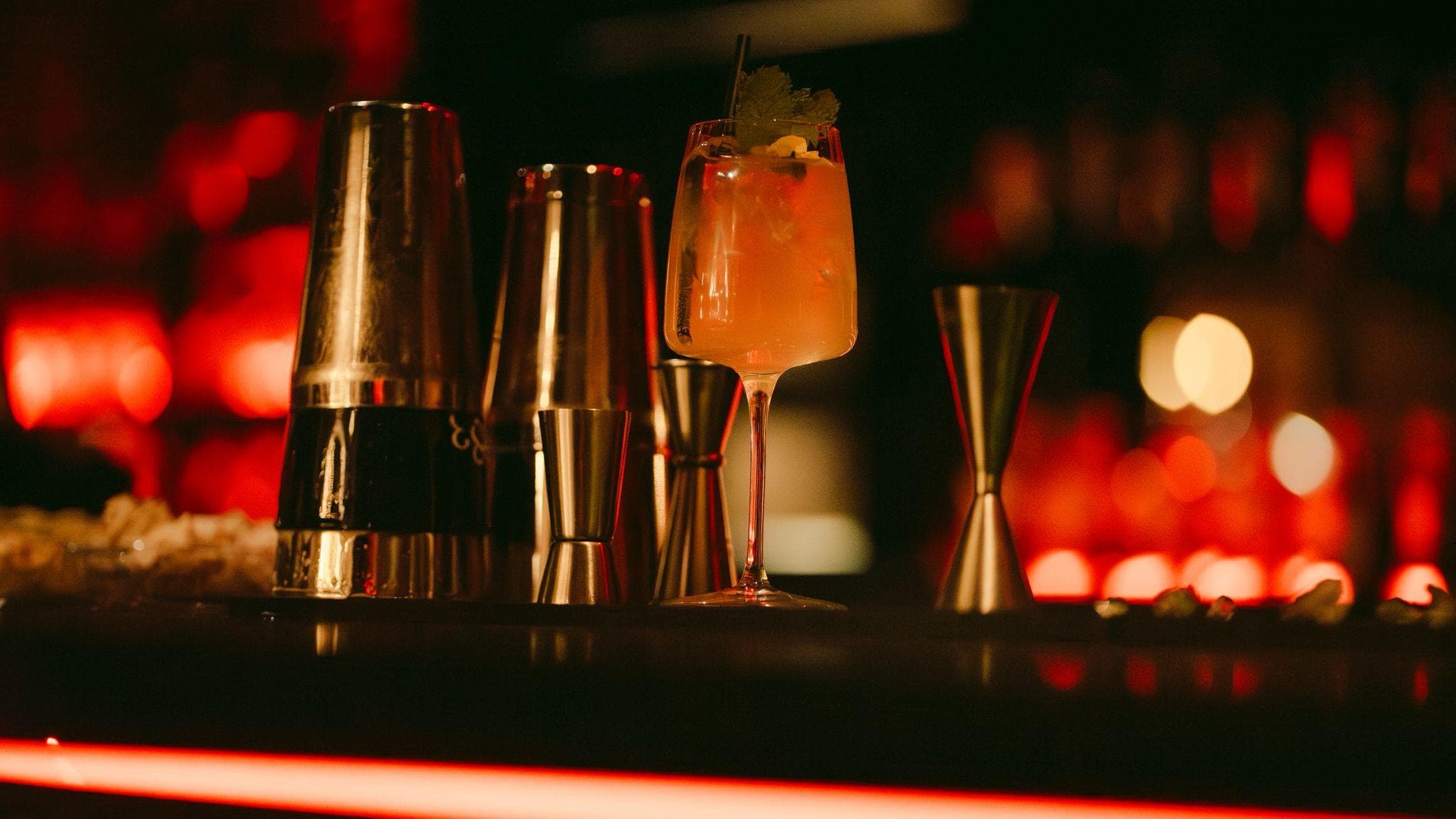 Shakers, jigger et cocktail orange alignés sur le comptoir éclairé de néon rouge