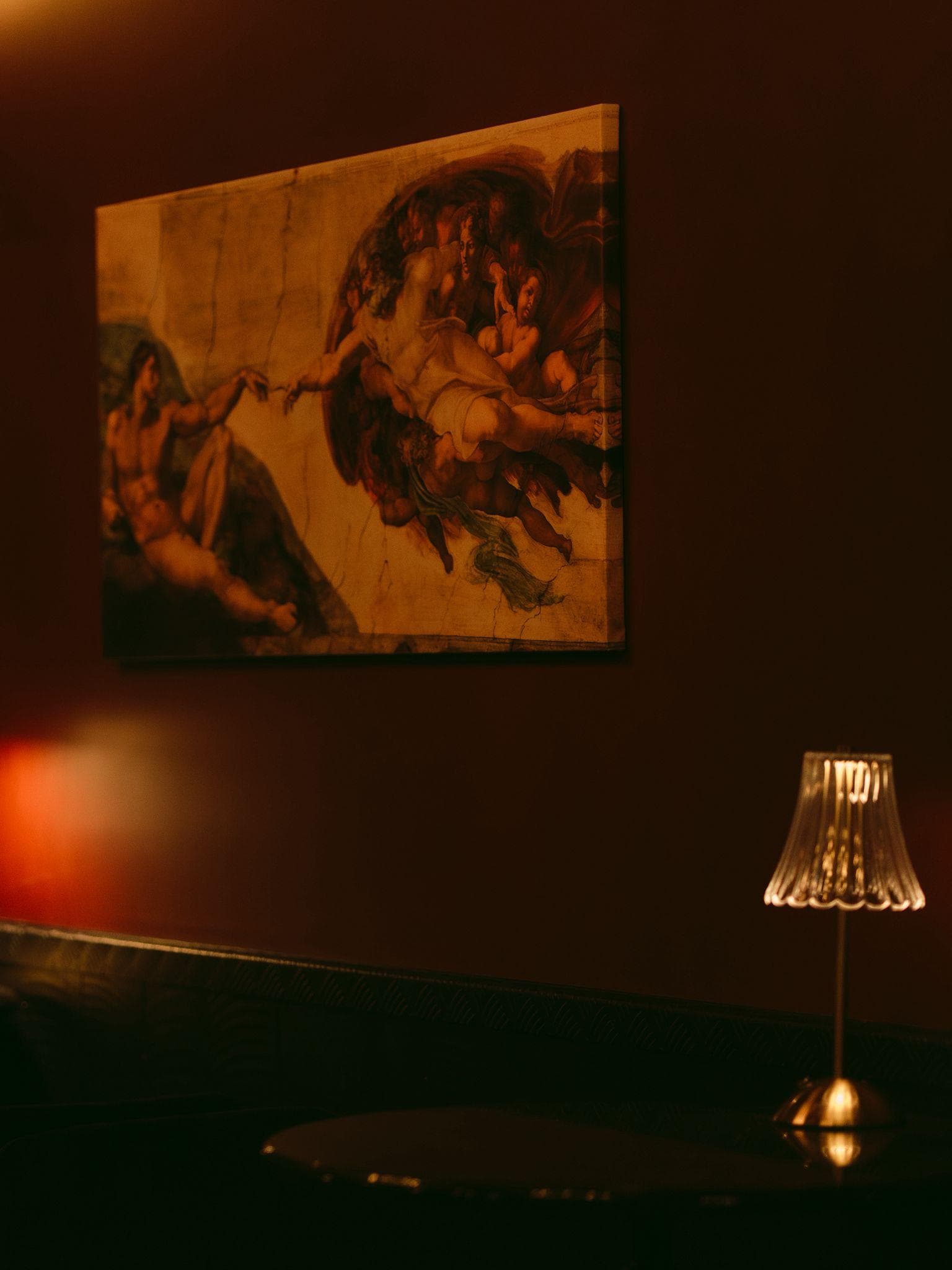Reproduction de La Création d'Adam accrochée au mur, éclairée par une lampe à franges