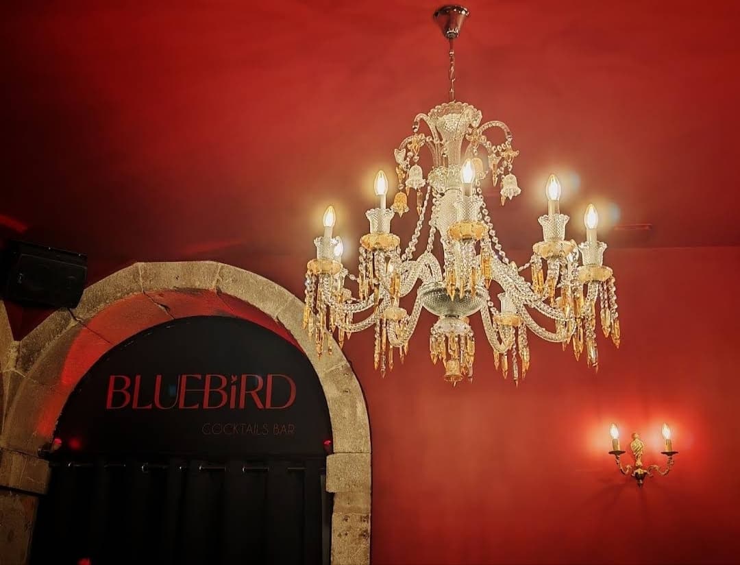 Porte noire du Bluebird sous une voûte de pierre, mur rouge et lustre de cristal