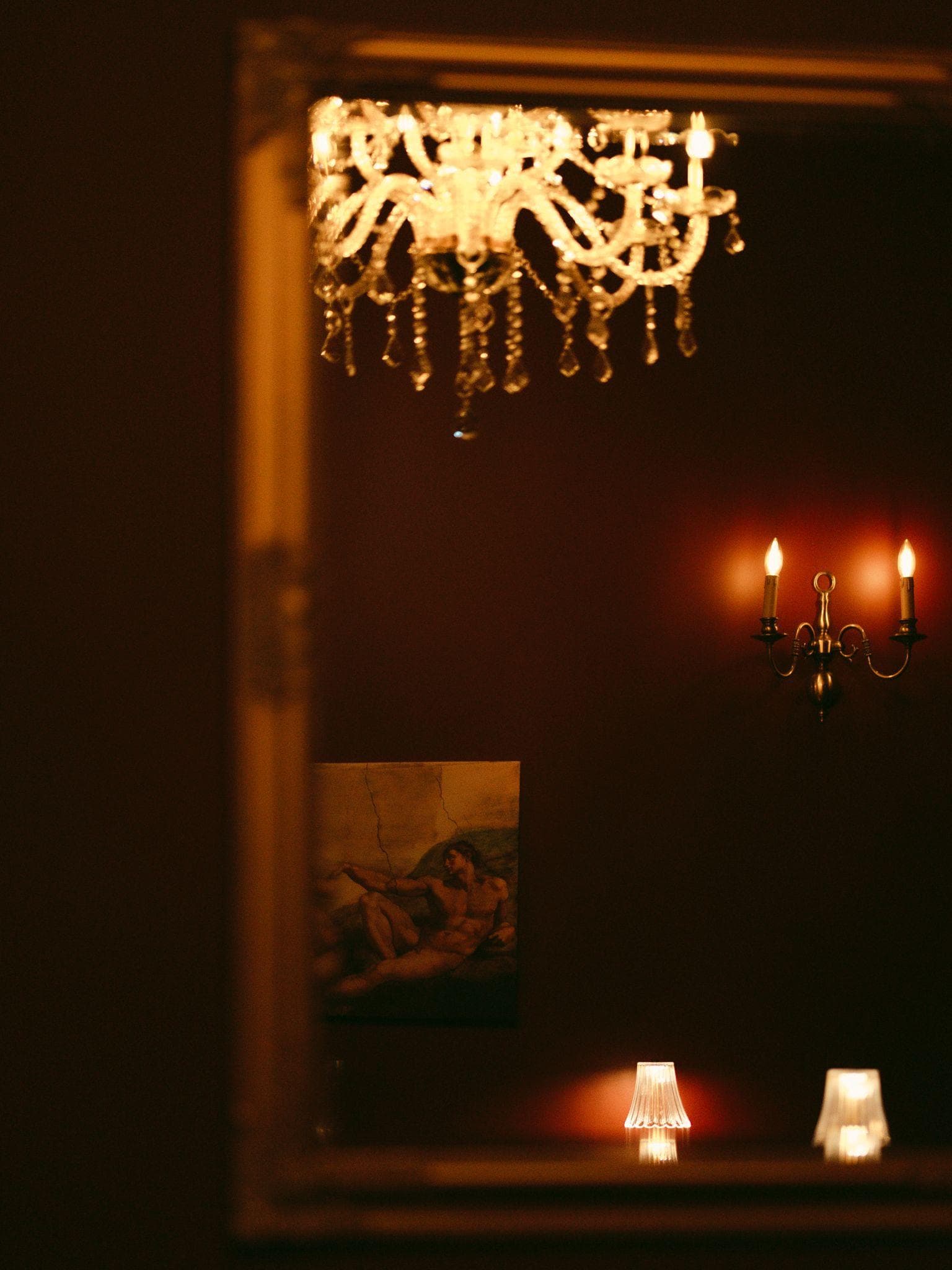 Miroir doré reflétant un lustre, une applique et deux lampes à abat-jour
