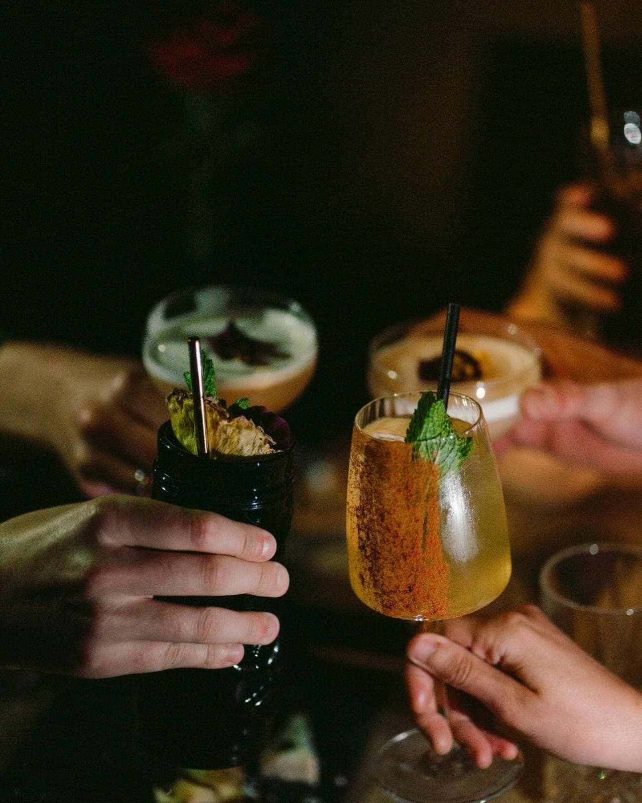 Plusieurs mains levant des cocktails pour trinquer autour d'une table